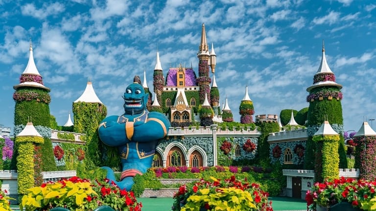 Dubai Miracle Garden with a floral castle, Aladdin's Genie statue, vibrant flowers, and whimsical structures under a blue sky.