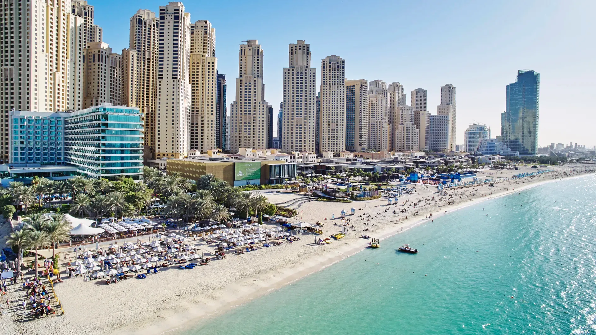 Jumeirah Beach in Dubai with luxury skyscrapers, palm trees, and a vibrant daytime beach scene with clear turquoise waters.