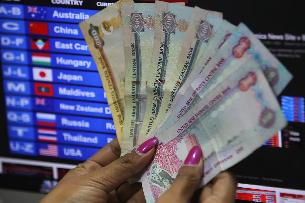 Hand holding UAE Dirham notes in front of currency exchange board