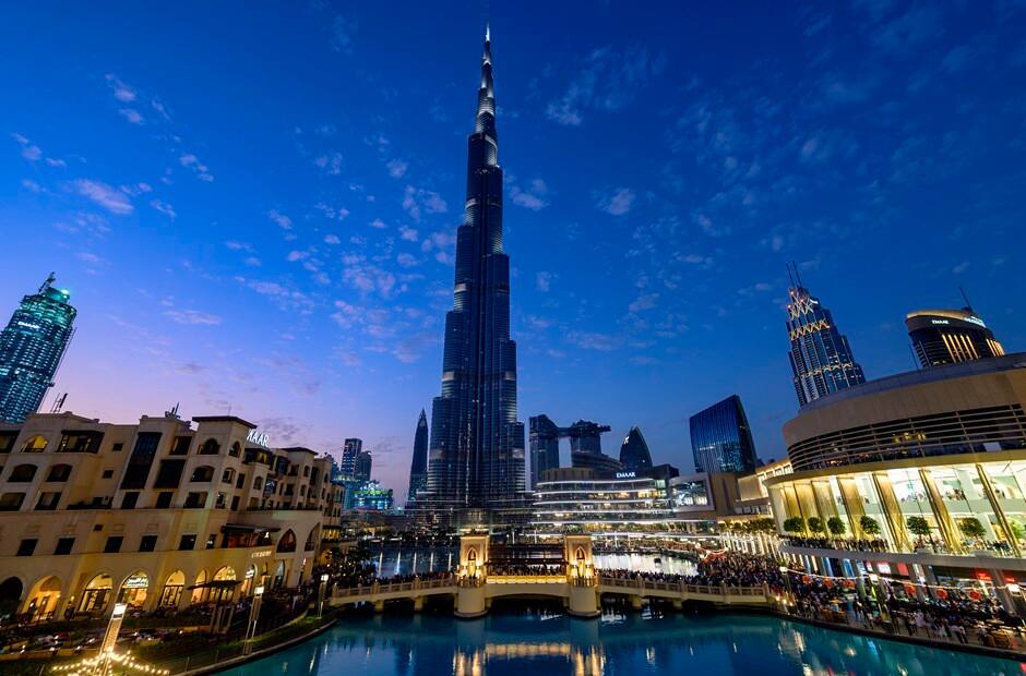 Burj Khalifa and Dubai Mall fountain area illuminated at night in Downtown Dubai with skyline in the background.
