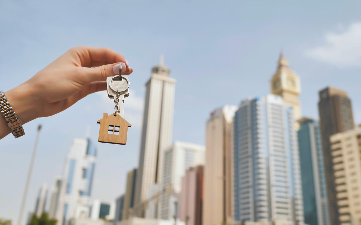 Hand holding house key with Dubai skyscrapers in the background, symbolizing buying property in the city’s real estate market.