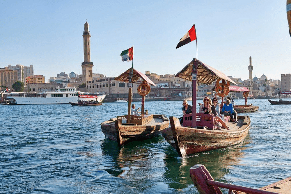 Tourists enjoying a traditional abra boat ride on Dubai Creek with Bur Dubai's old town architecture in the background.