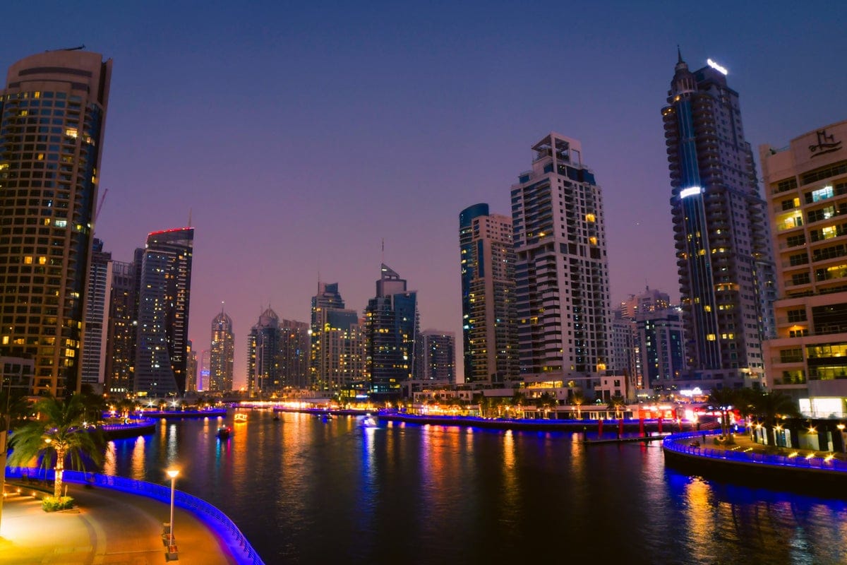 Dubai Marina at night with illuminated waterfront, modern skyscrapers, and city lights reflecting on the water.