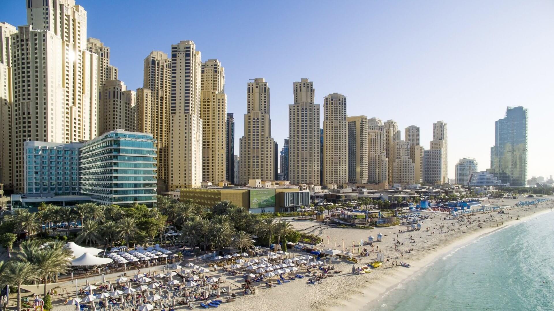 Jumeirah Beach Residence skyline with beachfront hotels, sun loungers, and clear blue water in Dubai.