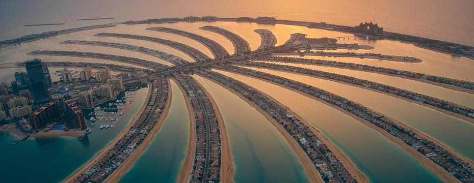 Aerial view of Palm Jumeirah in Dubai at sunset, showcasing luxury villas, resorts, and the iconic Atlantis hotel.