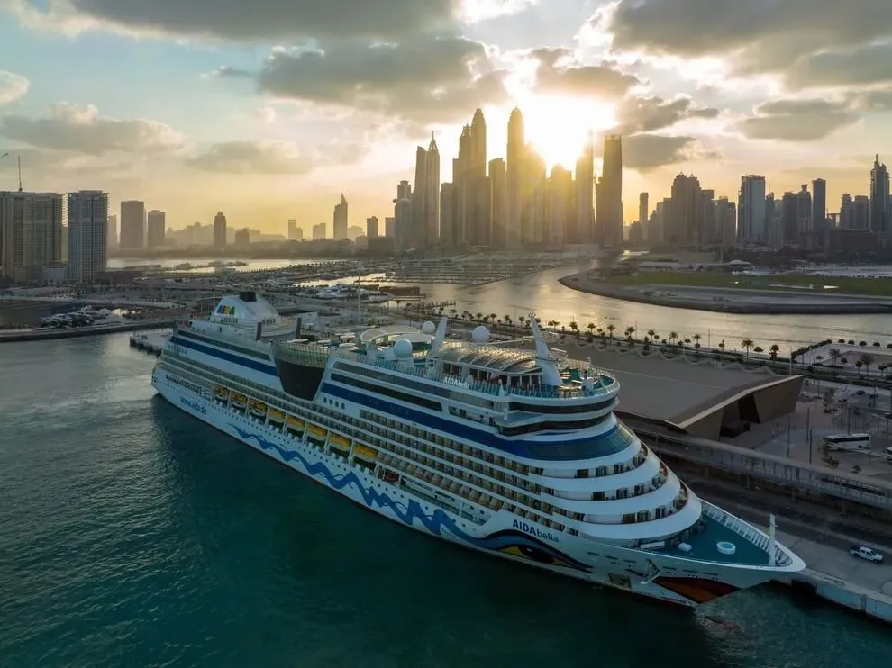 AIDA Bella cruise ship docked at Dubai Harbour Cruise Terminal with city skyline and sunset in the background
