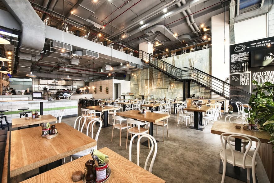 Modern industrial-style cafe interior with wooden tables, white chairs, and open kitchen at Tom & Serg Dubai