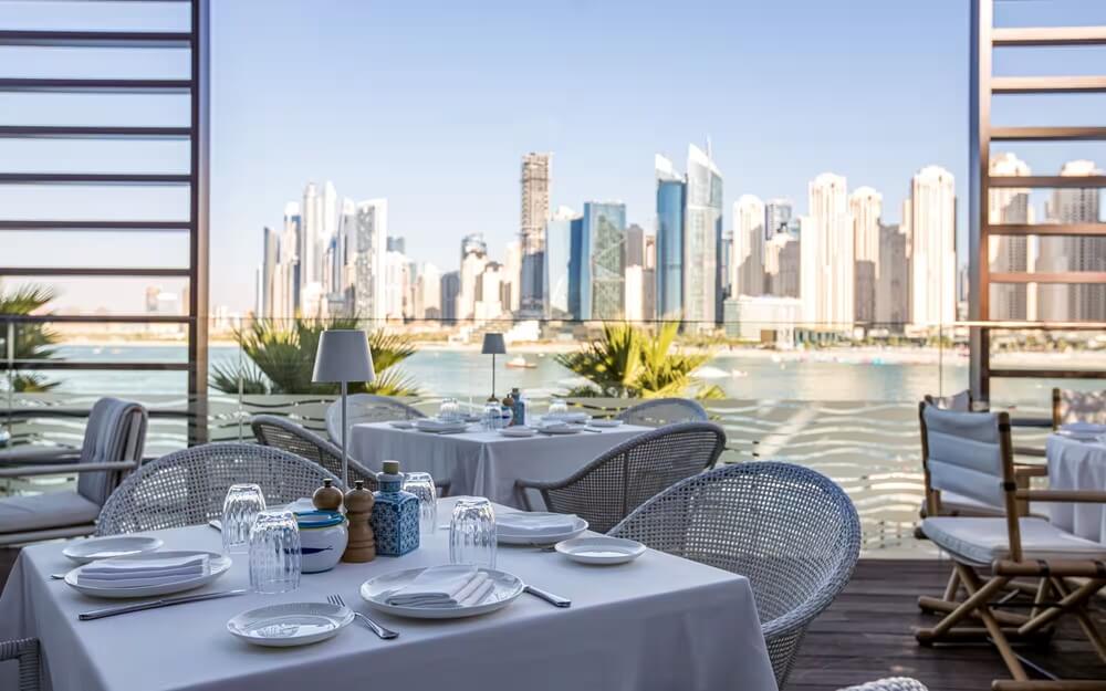 Elegant Dubai waterfront restaurant with marina skyline view and outdoor dining tables set for lunch or dinner