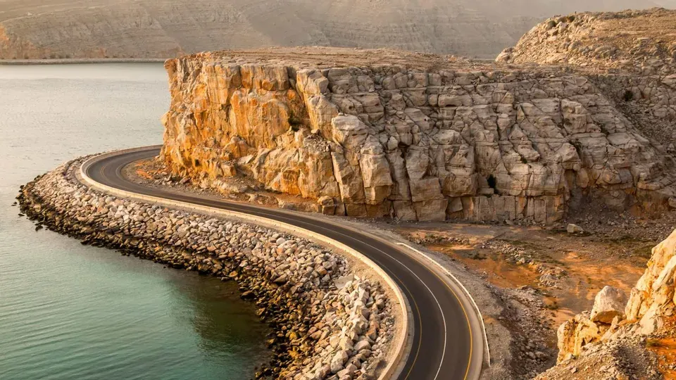 Scenic coastal road in Musandam, Oman with cliffs and water—popular route for road trips from Dubai.