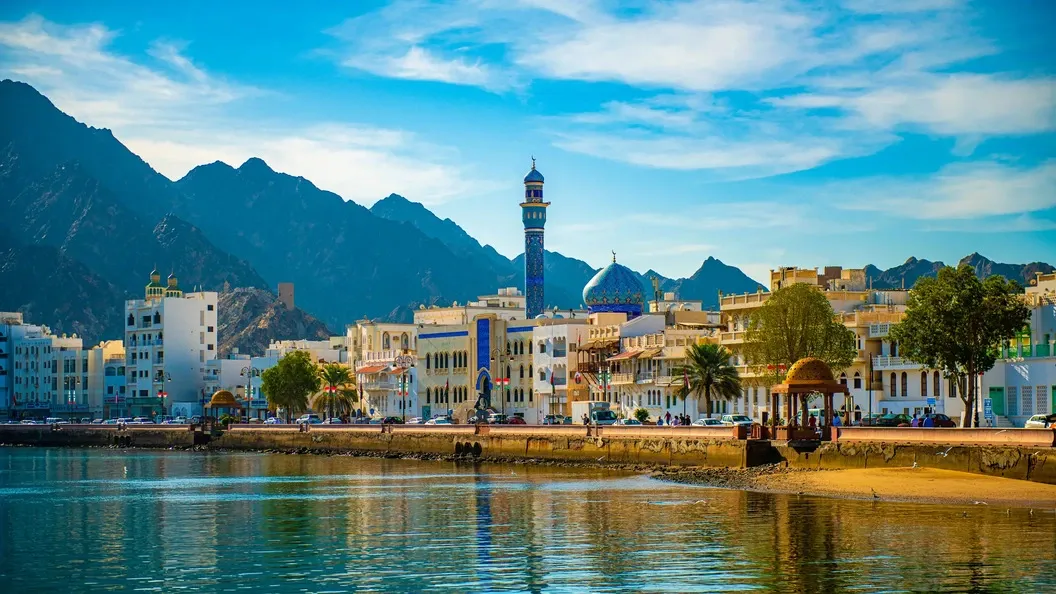 View of Muscat Corniche with waterfront, mosque, and mountains—a popular destination on road trips from Dubai to Oman.