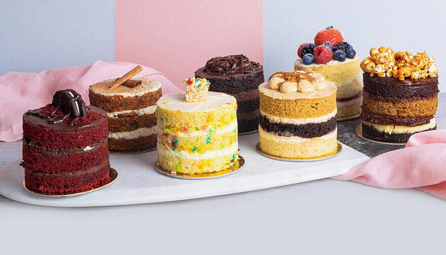 SugarMoo Dubai assorted mini layer cakes with toppings like berries, chocolate, and caramel popcorn