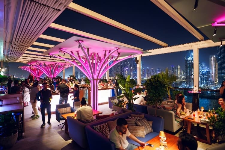 Above Eleven rooftop bar in Dubai with pink neon lighting, lively crowd, and Marina skyline views at night