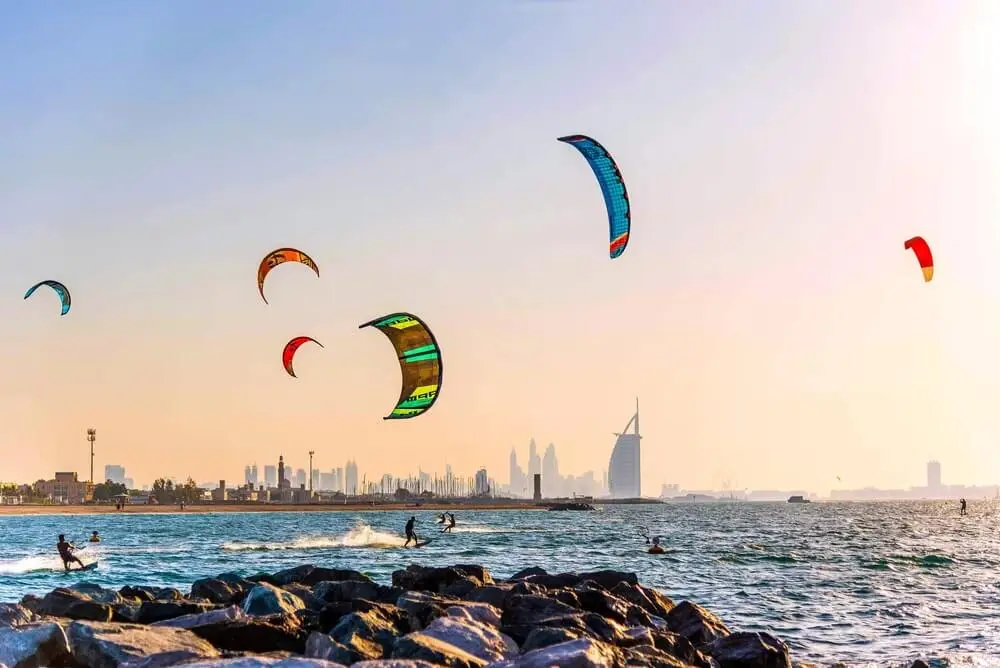 Colorful kitesurfers riding waves at Kite Beach Dubai with Burj Al Arab view, free beach activity for tourists