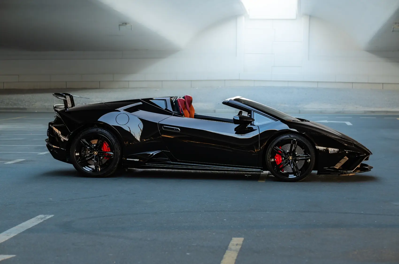 Side profile of black Lamborghini Huracán EVO Spyder with red calipers and red seats in Dubai for luxury car rental