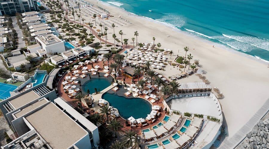 Aerial view of Nikki Beach Dubai with beachfront pool, sunbeds, and turquoise water at Pearl Jumeira