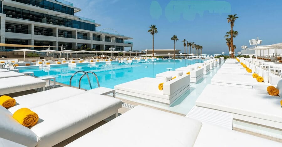 Luxury poolside beds with yellow towels at Playa Pacha, FIVE Luxe JBR, overlooking Dubai’s skyline and beachfront