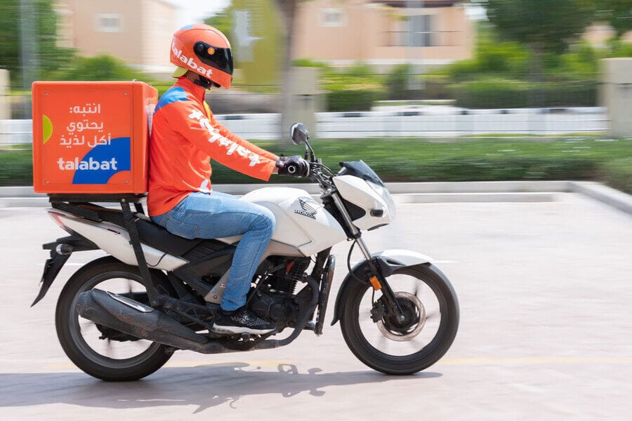 Talabat food delivery driver on motorbike wearing orange uniform in Dubai residential area.