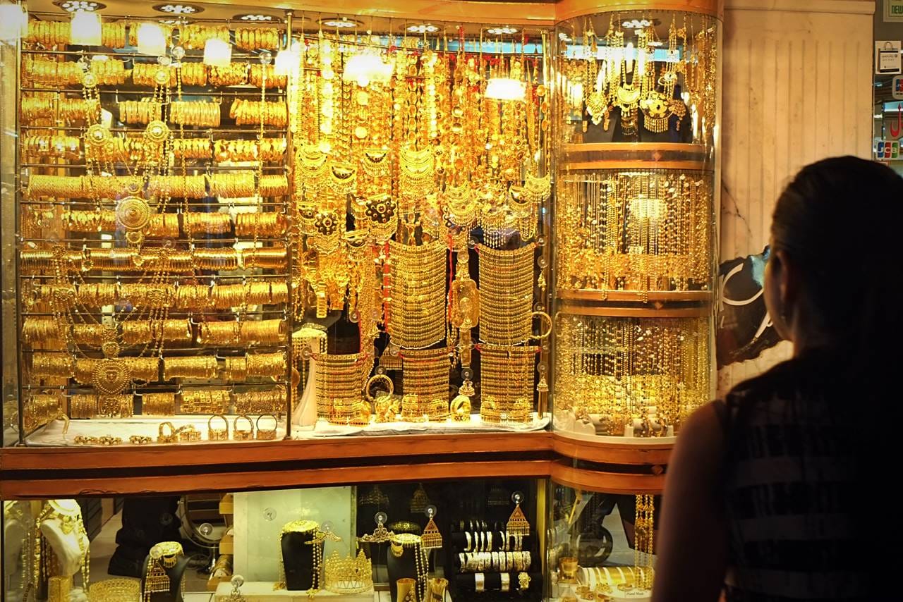 Shop window filled with gold jewelry at Dubai Deira Gold Souk with tourist looking at the display