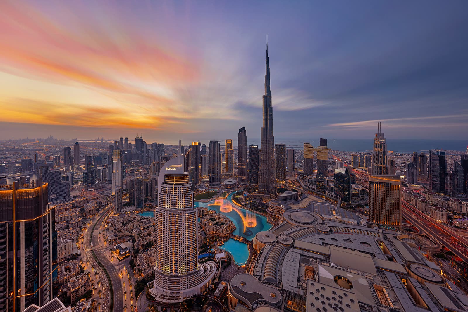 Aerial view of Downtown Dubai skyline with Burj Khalifa and Dubai Fountain at sunset.
