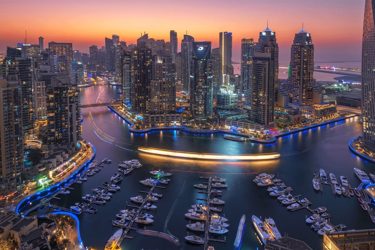 Dubai Marina at sunset with luxury yachts, skyscrapers, and vibrant nightlife lights reflecting on the water.
