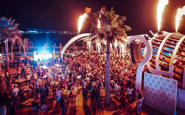 Massive beach club party in Dubai with fire shows, palm trees, and a vibrant crowd dancing under the night sky.