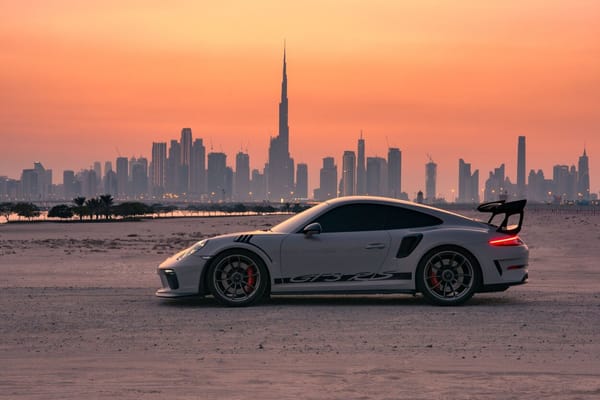 Porsche 911 GT3 RS parked in the Dubai desert at sunset with Burj Khalifa and city skyline in the background.