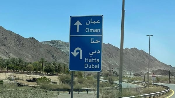 Directional road sign showing route to Oman and return to Hatta and Dubai near the UAE–Oman border crossing.