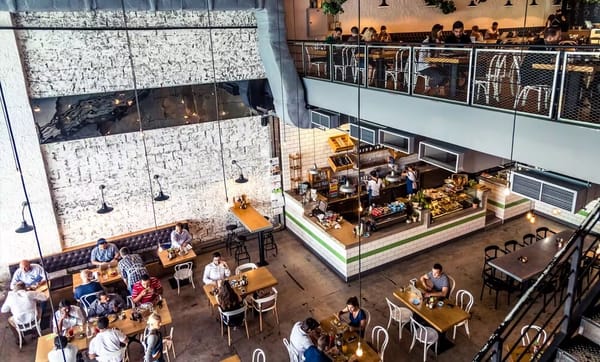 Aerial view of Tom & Serg Dubai cafe with open kitchen, industrial design, mezzanine seating, and diners