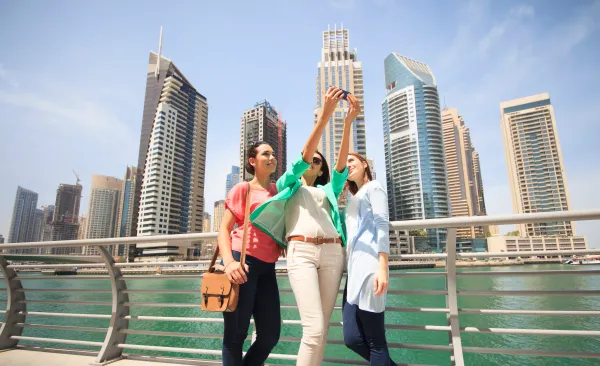 Three women taking a selfie in Dubai Marina, wearing modest casual outfits suitable for tourists